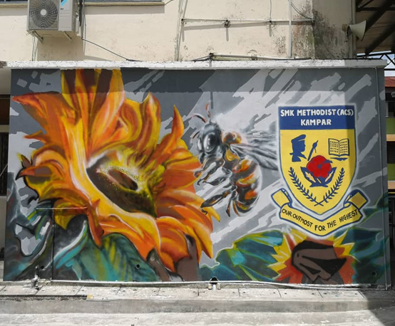 The mural features a prominent, vibrant yellow sunflower, on the left side, and a large bee on the right. The school’s logo is visible on the far right of the wall