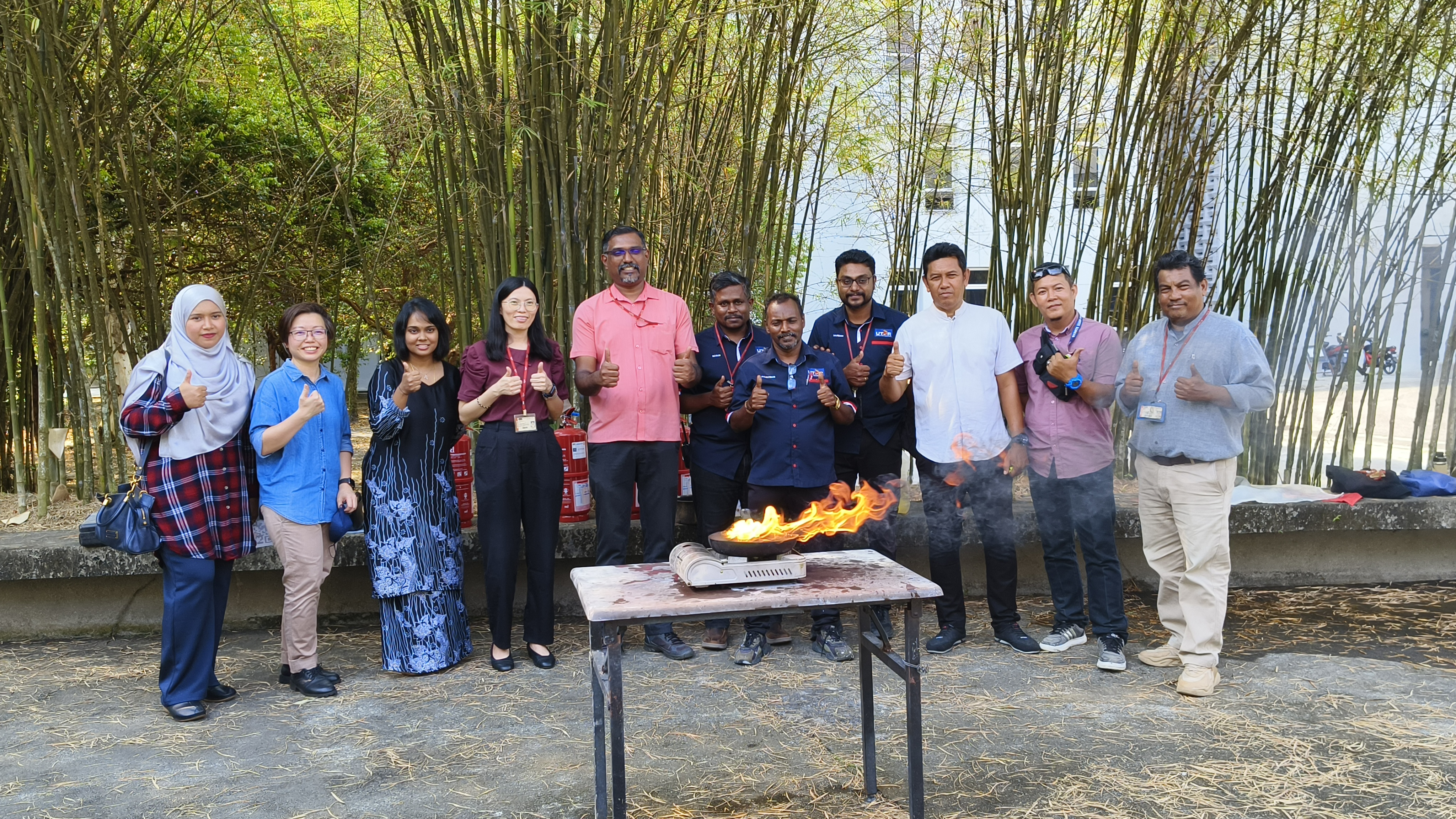 Fire is cool — but its a dangerous master. Even in a group photo, you can see (from left) Pn Nor Habibi Saadah, Ms Hoh, Ms Tulasi, Ms Ooi, Mr Prakash, Mr Manimaran, Mr Mahetiran, Mr Nareish Venu, En Ahmad Sabri, En Mohamad Saiful Nizam, and En Rosli standing a few feet away from the flames